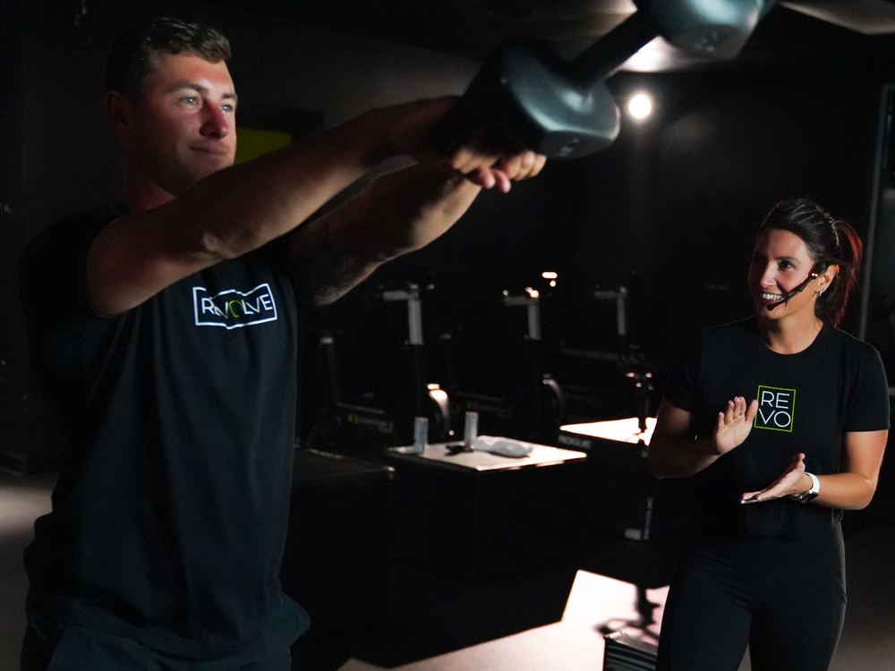 Revolve coach Megan cheering on a member during a kettlebell swing